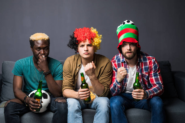 Ryhmä nuoria miehiä katsomassa jalkapalloa kotona ja juomassa olutta katsomassa televisiota.
 - Valokuva, kuva