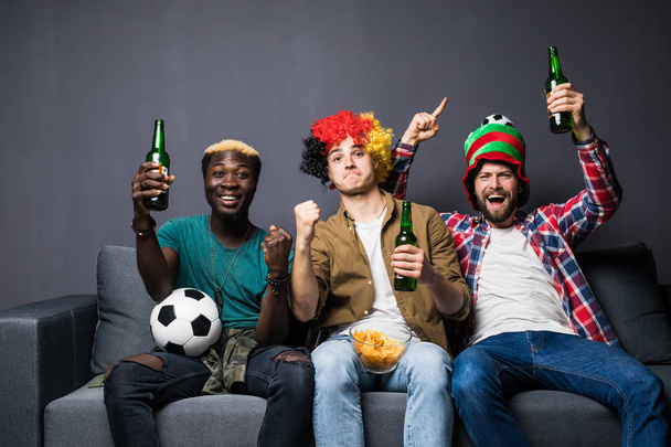 Три шанувальники друзі чоловіки дивляться футбол, кричать і кричать, п'ють пиво і їдять змій, сидячи на дивані вдома
. - Фото, зображення