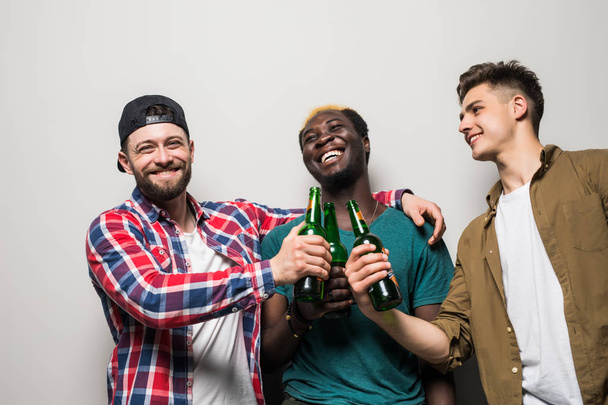 Three young joyful men holding beer and celebrating isolated over gray background - Photo, Image