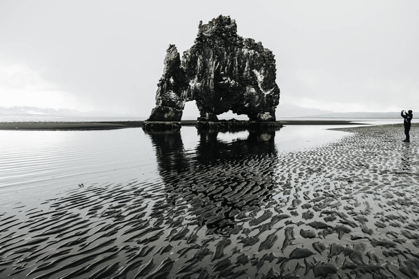 Man taking pictures of Hvitserkur - basalt rock in the form of a huge mammoth. The concept of extreme northern tourism. Northwest Iceland.  - Foto, Bild