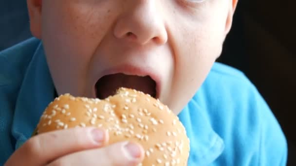 Egy tinédzser fiú eszik egy hamburgert gyorsétteremben közelében megtekintése. Egy fiú, aki eszik egy hamburgert száj - Felvétel, videó