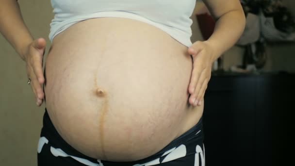 Close-up van een zwanger meisje in de negende maand van de zwangerschap maakt een massage van haar buik. - Video