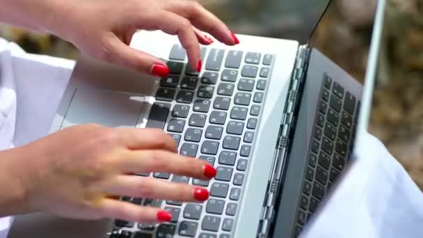 Nyáron szabadban. közeli a női kéz világos piros manikűr, és írja be a laptop billentyűzeten. működő-ra laptop. - Felvétel, videó