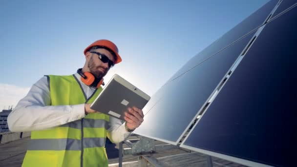 Een werknemer in de buurt van zonnepanelen, close-up. Ingenieur werken op zijn tablet naast de zonne-batterijen. - Video