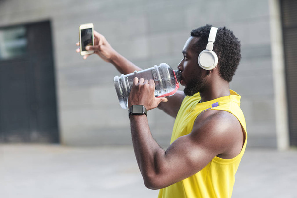 sporty man drinking water from bottle and taking selfie on smartphone  - Zdjęcie, obraz
