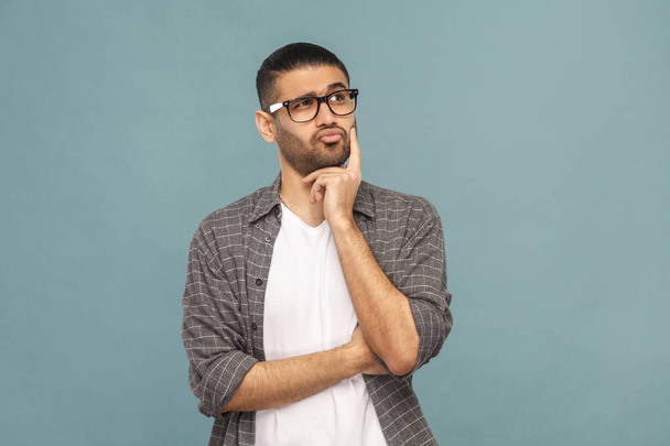 bearded pensive handsome man with black glasses in casual style posing on blue background. - 写真・画像