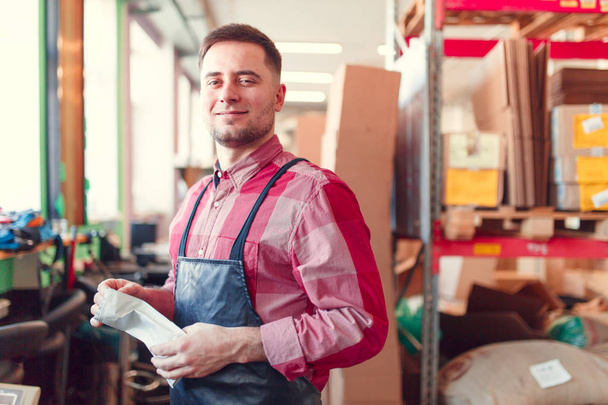 Picture of man in apron with bag in hands at shop for making coffee on background - Photo, Image