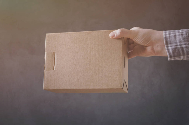 Main d'homme avec boîte en carton sur fond sombre
. - Photo, image