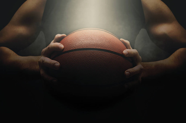 Joueur de basket masculin avec une balle sur fond sombre. S'adapter jeune homme en tenue de sport tenant basket-ball
. - Photo, image