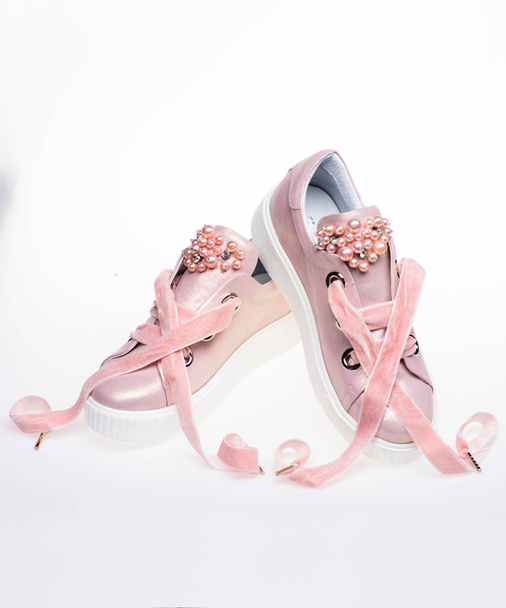 Cute shoes isolated on white background. Footwear for girls and women decorated with pearl beads. Femininity concept. Pair of pale pink female sneakers with velvet ribbons - Fotoğraf, Görsel
