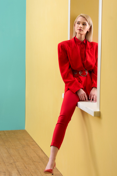 beautiful pensive woman in stylish red suit sitting on decorative window - 写真・画像