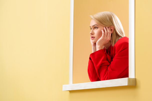 young fashionable woman in red suit looking out decorative window - Foto, afbeelding