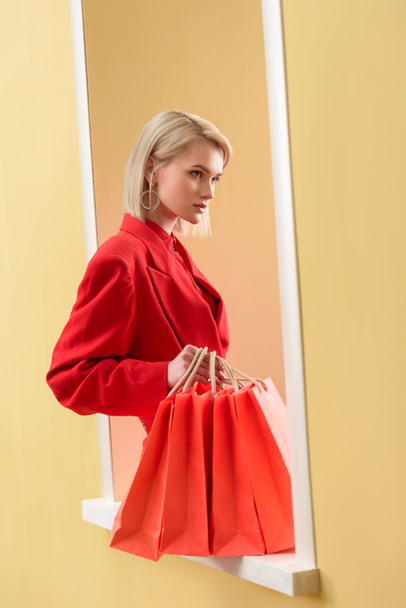young fashionable woman in red clothing with red shopping bags sitting on decorative window - Foto, imagen