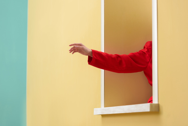 cropped shot of woman in red jacket sticking hand out decorative window - Foto, Imagem