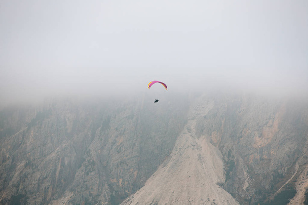 Paralotnia latająca nad górami w dolomitach we Włoszech. Słoneczny jesienny dzień. - Zdjęcie, obraz