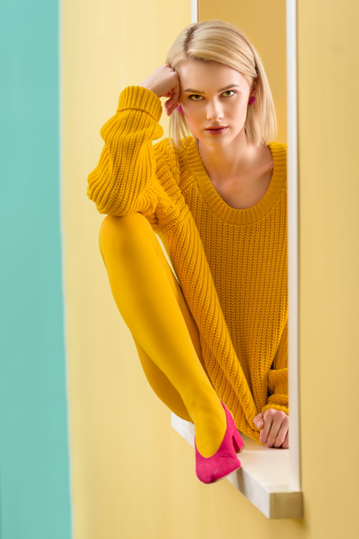 стильний блондин жінка в жовтий светр, сидячи на оздоблене вікно - Фото, зображення