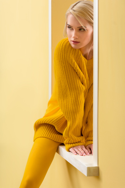 partial view of stylish pensive woman in yellow sweater and tights sitting on decorative window - 写真・画像