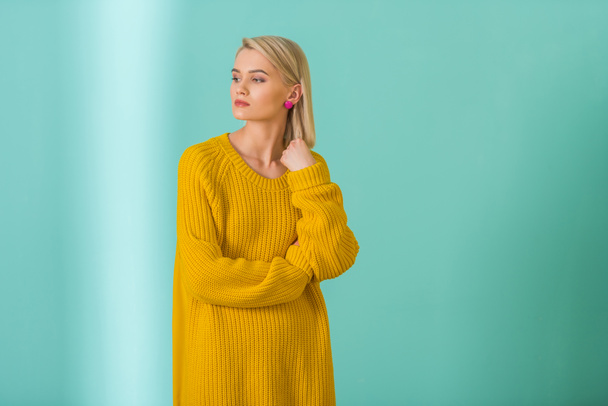 portrait of beautiful pensive woman in yellow sweater posing on blue background - Foto, Imagem