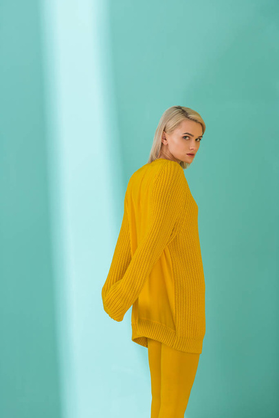 side view of young woman in yellow sweater and tights posing on blue background - Foto, Bild