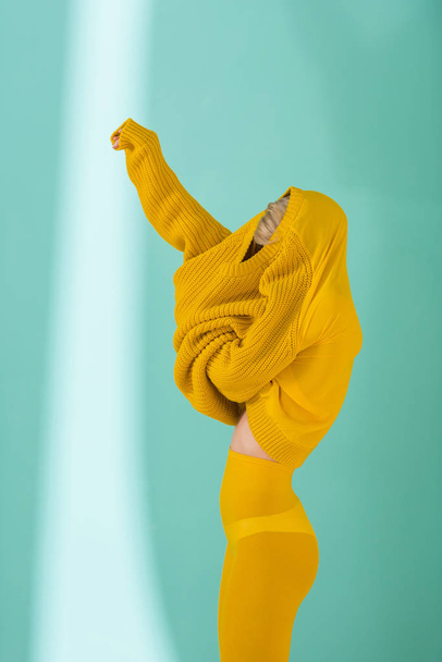 side view of woman in yellow tights wearing yellow sweater posing on blue background - Foto, Imagem