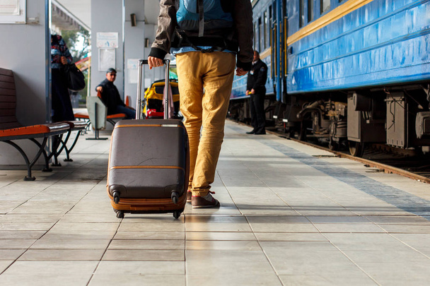 旅行の概念。男性スニーカー靴を履くと黄色のパンツの茶色の荷物を持って旅行やバックパックは鉄道駅。晴れた日. - 写真・画像