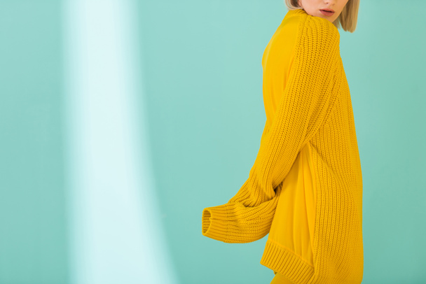 partial view of woman in yellow sweater posing on blue background - Photo, Image