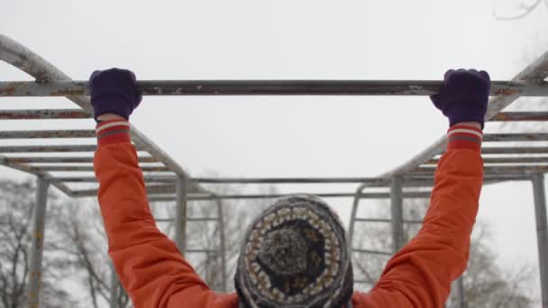 Hombre joven en chaqueta naranja haciendo pullups en barras horizontales al aire libre en invierno
 - Metraje, vídeo
