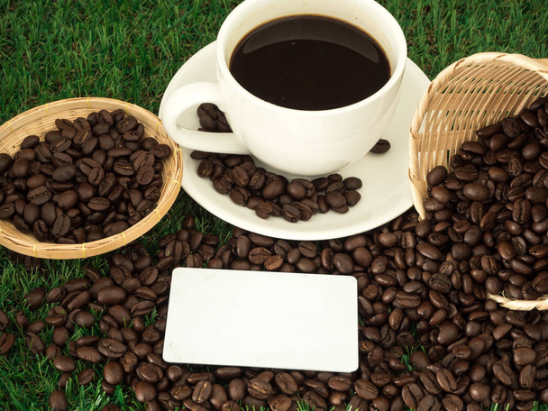 Φλιτζάνι καφέ και καφέ φασόλια σε ξύλινη κουτάλα και μπισκότο σε γρασίδι πράσινο φόντο - Φωτογραφία, εικόνα
