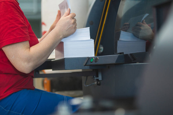 Stack of paper in hands of female worker in front of printing press machine - Photo, Image