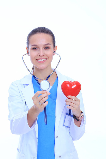 Positive female doctor standing with stethoscope and red heart symbol isolated. Woman doctor - Φωτογραφία, εικόνα