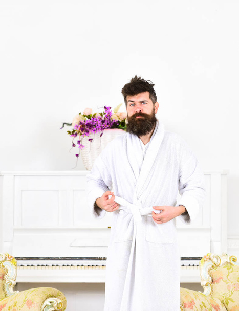 Sleepy guy frowning and raising his eyebrows. Man in bathrobe standing in front of piano. Tired hipster in his apartment - Fotografie, Obrázek