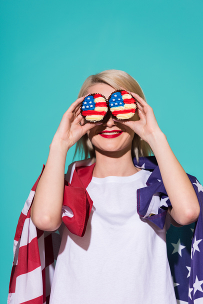 zasłonięte widok uśmiechający się kobieta z amerykańską flagę i babeczki na niebieskim tle, z okazji 4 lipca koncepcja - Zdjęcie, obraz