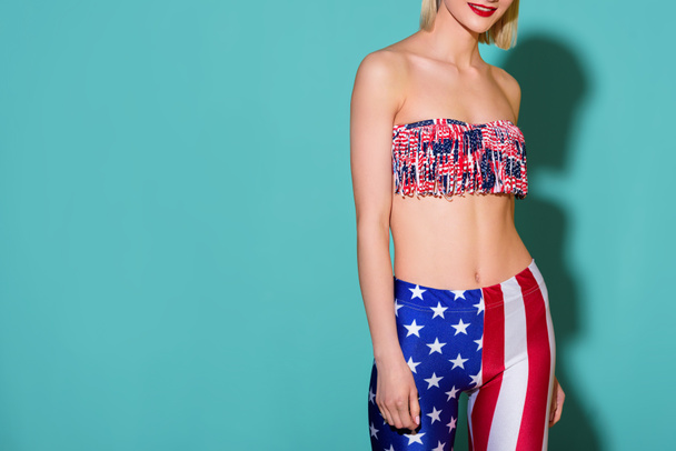 cropped shot of smiling woman in top and leggings with american flag pattern posing on blue background - Foto, Imagen