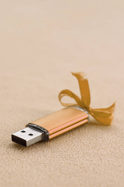 Оранжевый USB флэш-карты памяти с голубым луком лежит на одеяле из мягкой и пушистой светло-оранжевой ткани флис. Классический женский подарок для карты памяти
 - Фото, изображение