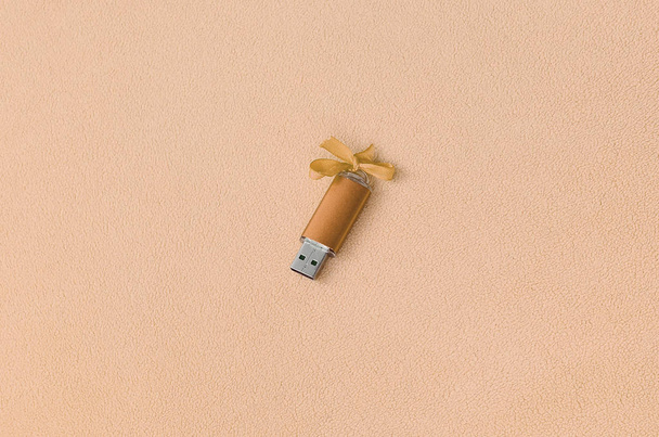 Помаранчева картка флеш-пам'яті USB з бантом лежить на ковдрі м'якої та пухнастої легкої помаранчевої тканини флісу. Класичний жіночий дизайн подарункової картки пам'яті
 - Фото, зображення