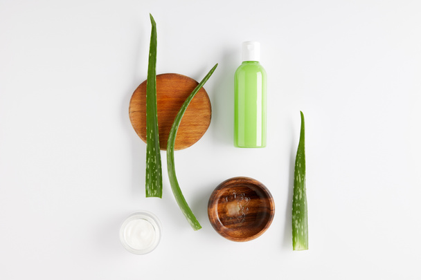 top view of wooden bowl with aloe vera juice, organic cream and shower gel, aloe vera leaves on wooden slices  - Foto, afbeelding
