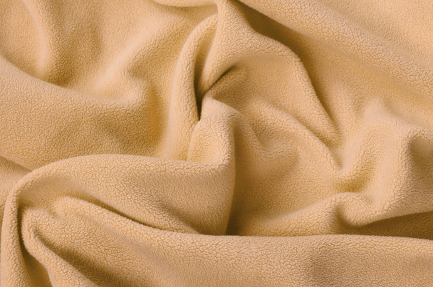 die Decke aus pelzig orangefarbenem Fleece-Stoff. ein Hintergrund aus hellorangefarbenem weichem Plüsch-Fleece-Material mit vielen Relieffalten - Foto, Bild