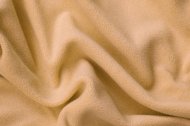 die Decke aus pelzig orangefarbenem Fleece-Stoff. ein Hintergrund aus hellorangefarbenem weichem Plüsch-Fleece-Material mit vielen Relieffalten - Foto, Bild