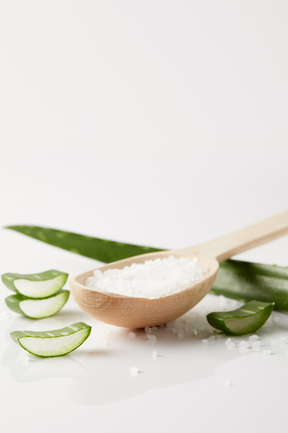 close up image of wooden spoon with salt, aloe vera leaf and slices on white surface - Фото, изображение