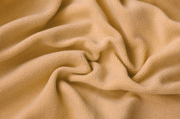 The blanket of furry orange fleece fabric. A background of light orange soft plush fleece material with a lot of relief folds - Photo, Image