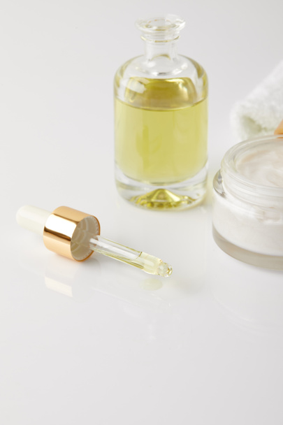 Close-up beeld van organische room in container, fles cosmetische olie, pipet en witte handdoek  - Foto, afbeelding