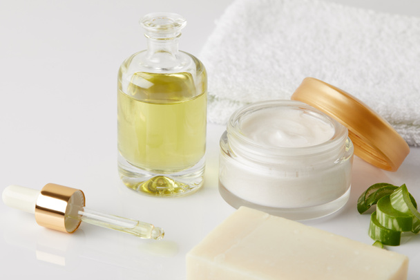 Close-up shot van de cosmetische olie met druppelaar, zeep, handdoek, organische crème in container en aloë vera plakjes  - Foto, afbeelding