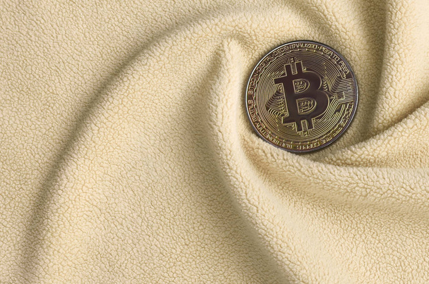 Το golden bitcoin βρίσκεται σε ένα κάλυμμα από ύφασμα μαλακό και αφράτο ελαφρύ fleece πορτοκαλί με ένα μεγάλο αριθμό ανακούφιση πτυχώσεις. Το σχήμα του πτυχώσεις μοιάζει με έναν ανεμιστήρα από μια κάρτα βίντεο πιο δροσερές - Φωτογραφία, εικόνα