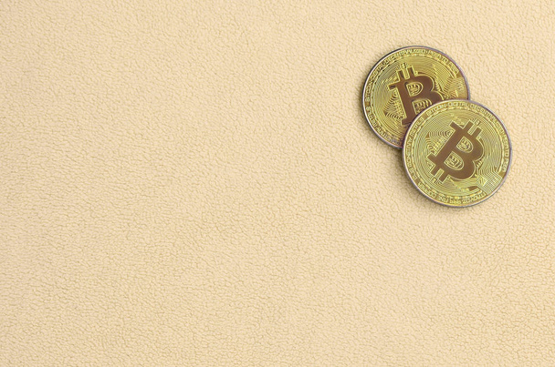 Dos bitcoins de oro se encuentra en una manta hecha de suave y esponjosa tela de lana naranja claro. Visualización física de la moneda criptográfica virtual
 - Foto, Imagen