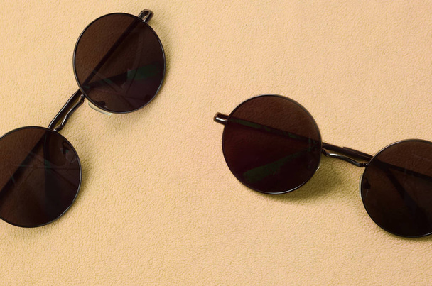 Dwa stylowe czarne okulary przeciwsłoneczne z okrągłe okulary leży na kocu wykonane z tkaniny miękkie i puszyste jasny pomarańczowy Polar. Obraz tła modne kolory moda - Zdjęcie, obraz