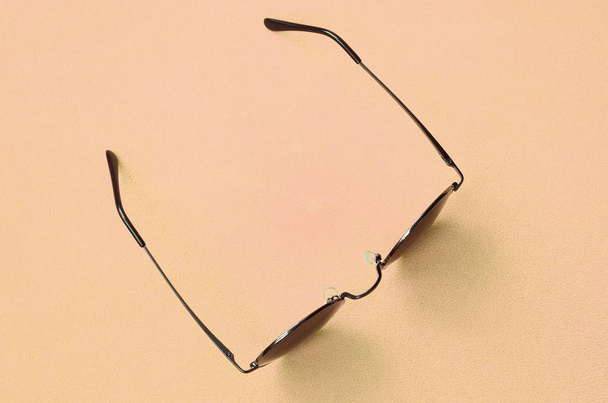 Die stylische schwarze Sonnenbrille mit runder Brille liegt auf einer Decke aus weichem und flauschigem hellorangefarbenem Fleece-Stoff. modisches Hintergrundbild in modischen Farben - Foto, Bild