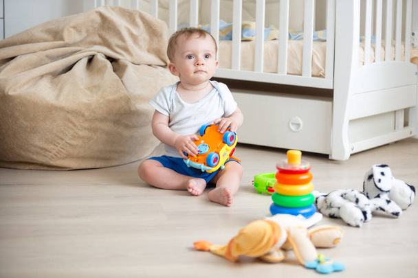 10 months old baby boy sitting on wooden floor at bedroom and playing with toys - Photo, Image