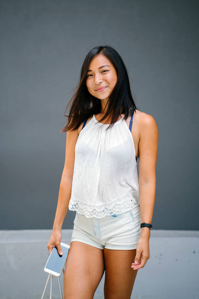 Portrait of a cute, athletic, tanned Asian Chinese girl walking on the street against a grey background. - Φωτογραφία, εικόνα
