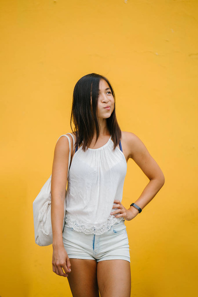 Portrait of an athletic, cute Chinese Asian girl dressed comfortably and smiling at the camera against a yellow background in a studio. - Foto, Imagem
