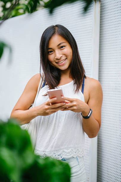 Athletic, toned and tanned Chinese Asian girl smiling as she texts on her mobile phone in the day. She is relaxed and having fun. - Fotó, kép